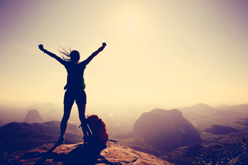 Person standing with arms raised at sunrise
